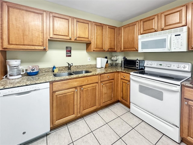 kitchen featuring dark stone countertops, sink, light tile patterned flooring, and white appliances