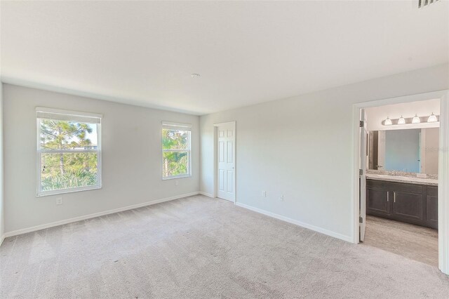 unfurnished bedroom featuring light colored carpet, a sink, baseboards, and ensuite bathroom