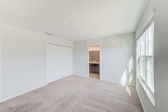 unfurnished bedroom featuring a closet, visible vents, light carpet, ensuite bath, and baseboards