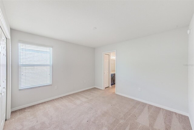 unfurnished bedroom featuring light colored carpet, ensuite bath, and baseboards