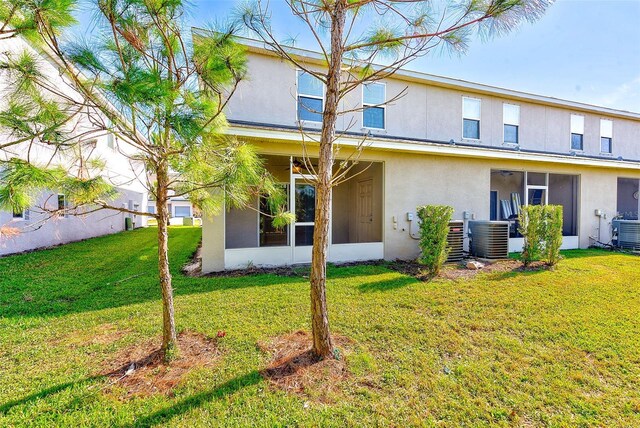 rear view of property featuring a sunroom, central AC unit, a lawn, and stucco siding