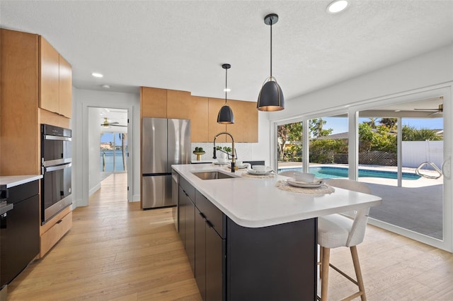 kitchen with ceiling fan, sink, hanging light fixtures, stainless steel appliances, and a kitchen island with sink