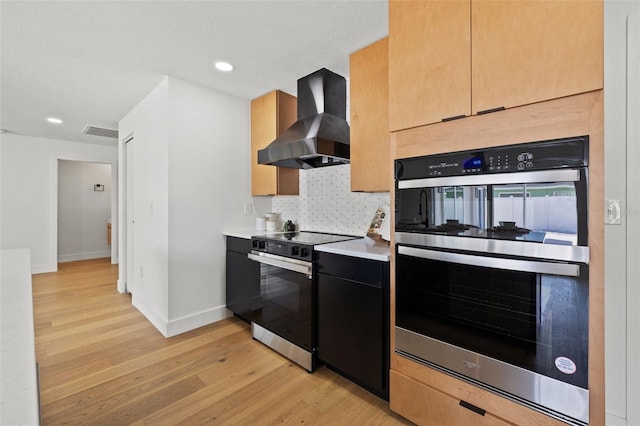 kitchen featuring light brown cabinetry, stainless steel appliances, light hardwood / wood-style flooring, and wall chimney range hood