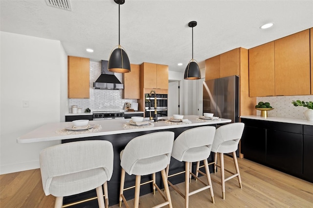 kitchen with backsplash, wall chimney exhaust hood, pendant lighting, and light wood-type flooring