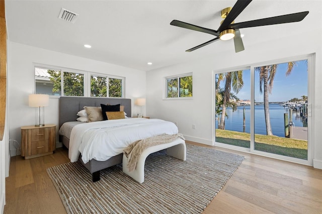 bedroom with access to exterior, light wood-type flooring, a water view, and ceiling fan