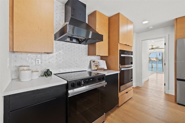 kitchen featuring decorative backsplash, wall chimney exhaust hood, stainless steel appliances, and light hardwood / wood-style floors