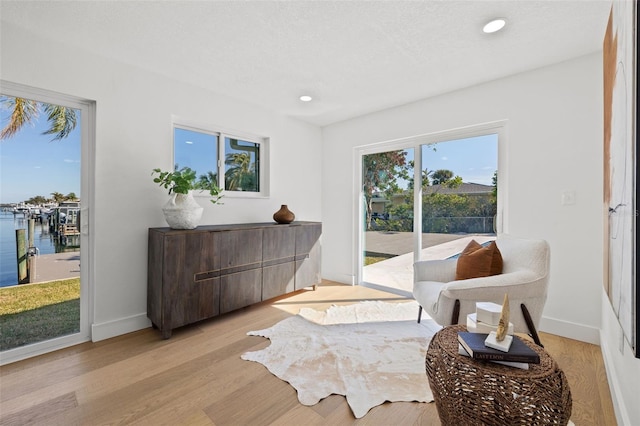 sitting room featuring a water view, a textured ceiling, and light hardwood / wood-style flooring