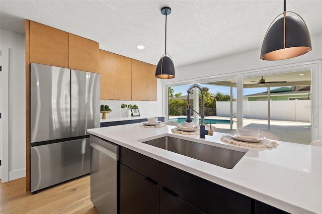 kitchen with backsplash, stainless steel appliances, sink, pendant lighting, and light hardwood / wood-style flooring