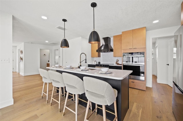 kitchen featuring pendant lighting, stainless steel double oven, premium range hood, and light hardwood / wood-style flooring