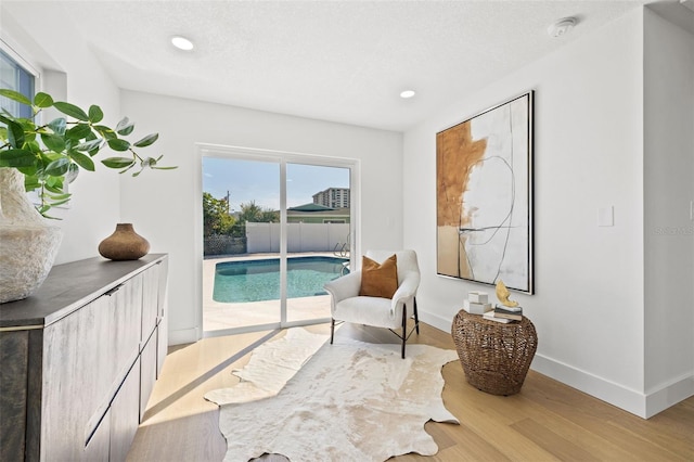 living area with a textured ceiling, light hardwood / wood-style floors, and a swimming pool