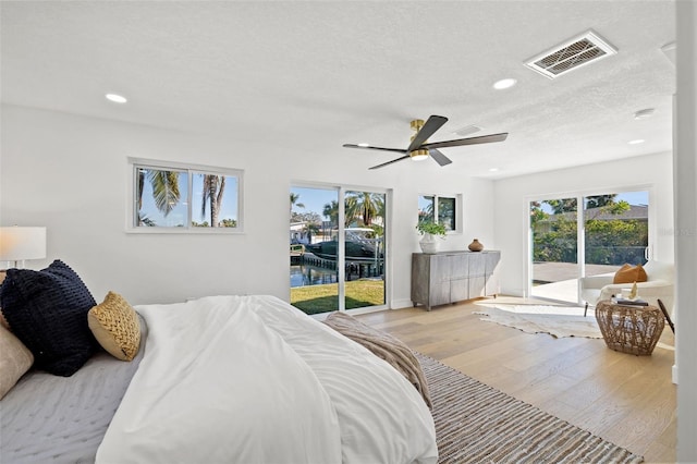 bedroom with a water view, light hardwood / wood-style flooring, ceiling fan, access to exterior, and a textured ceiling