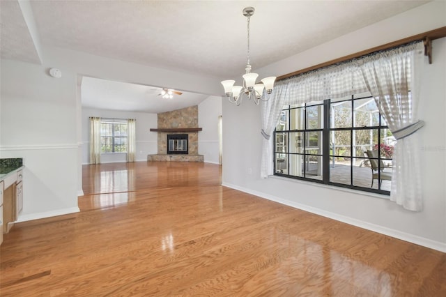 unfurnished living room with hardwood / wood-style flooring, ceiling fan with notable chandelier, a fireplace, and vaulted ceiling