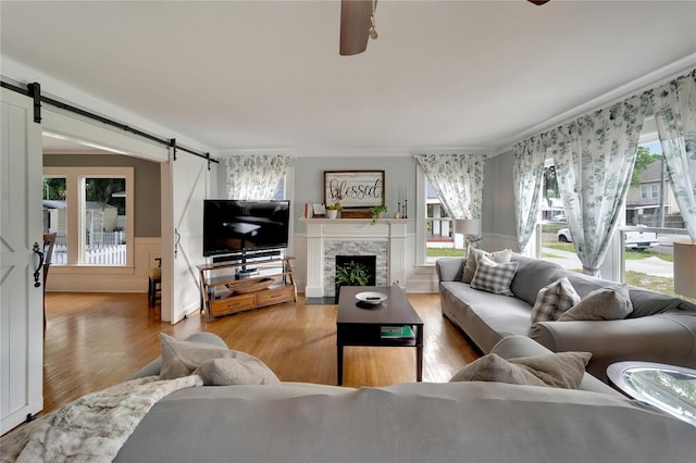 living room featuring ceiling fan, a barn door, crown molding, wood-type flooring, and a fireplace