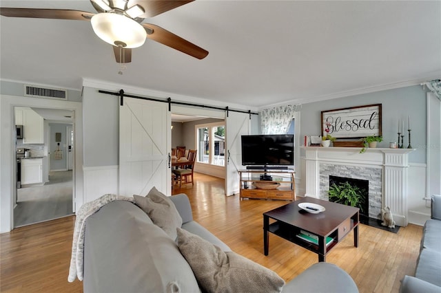 living room featuring light wood-type flooring, ornamental molding, ceiling fan, a barn door, and a fireplace