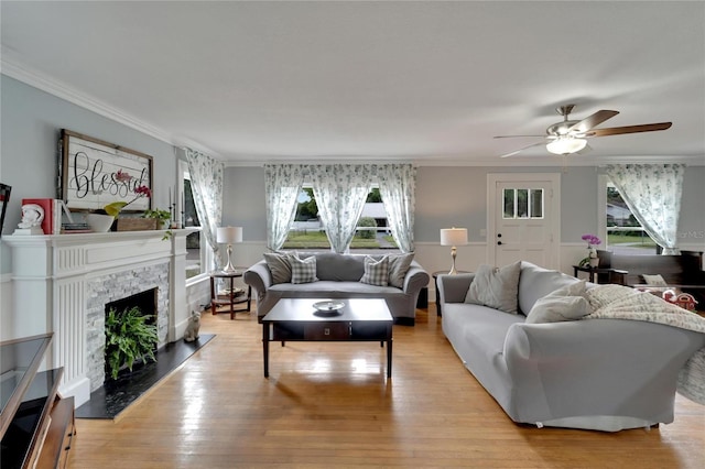 living room with a stone fireplace, crown molding, light hardwood / wood-style flooring, and a healthy amount of sunlight