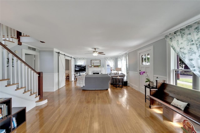 living room featuring ceiling fan, a barn door, light wood-type flooring, and crown molding