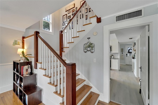 staircase with wood-type flooring and crown molding