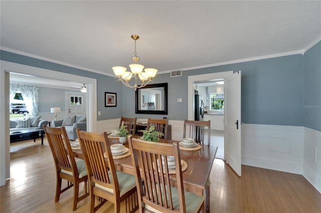 dining area featuring light wood-type flooring, ornamental molding, and an inviting chandelier