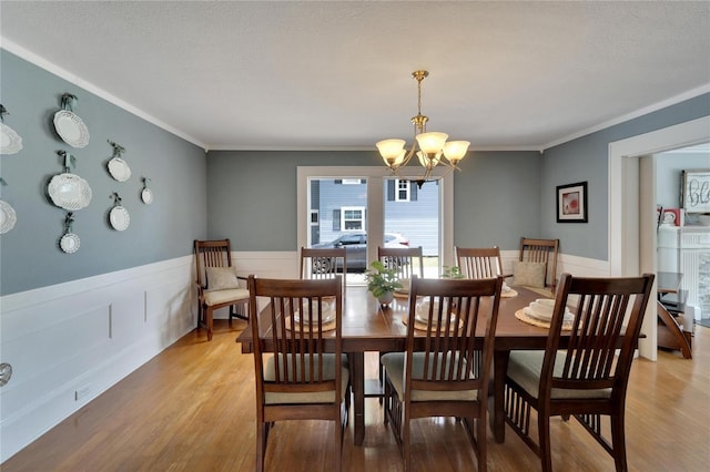 dining area with crown molding, light hardwood / wood-style floors, a textured ceiling, and an inviting chandelier