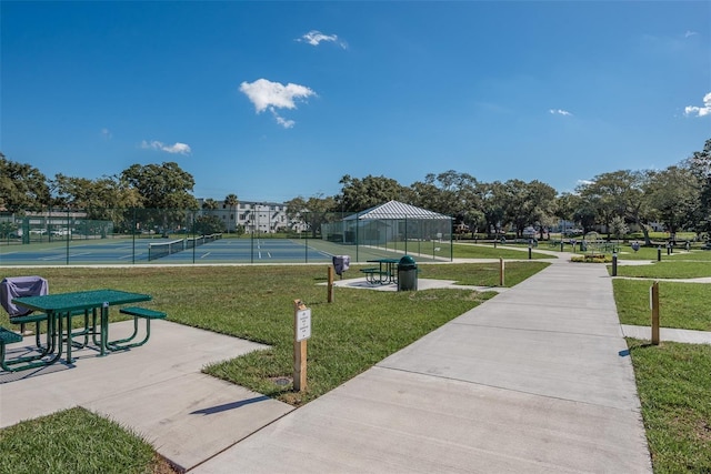 view of property's community with a lawn and tennis court