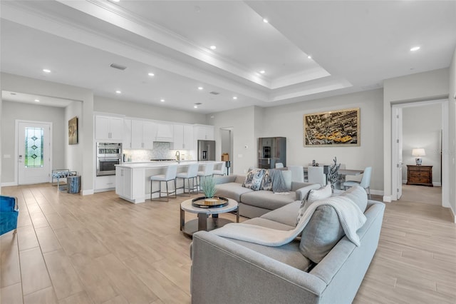 living room with a raised ceiling, sink, crown molding, and light hardwood / wood-style flooring