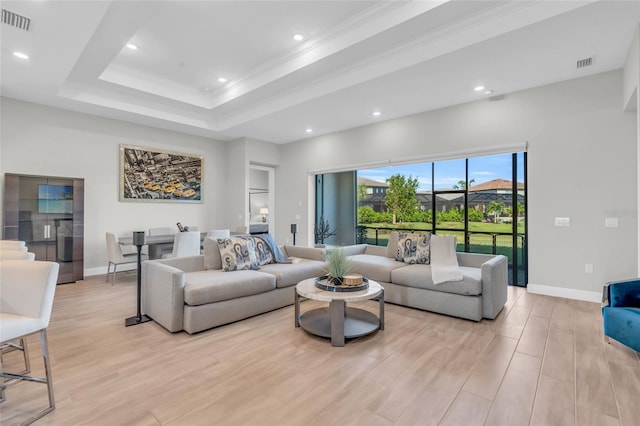 living room featuring a raised ceiling, ornamental molding, and light hardwood / wood-style flooring