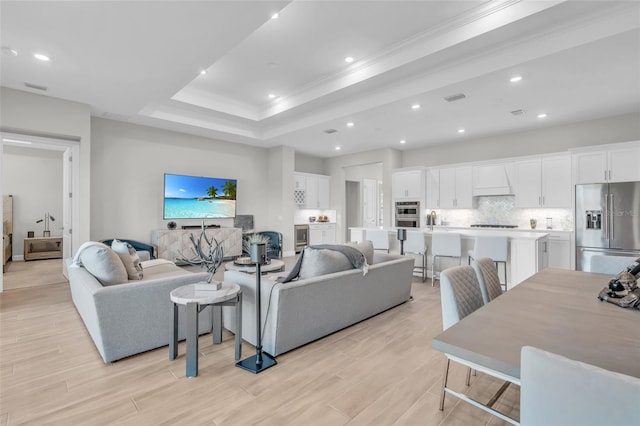 living room featuring crown molding, a tray ceiling, and light hardwood / wood-style flooring