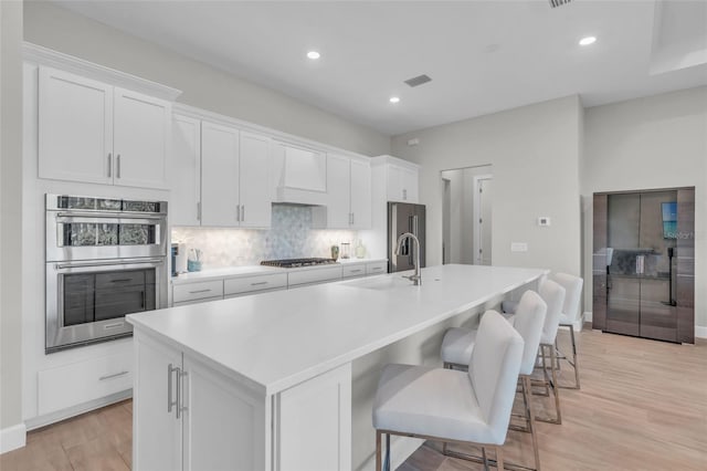 kitchen featuring a kitchen island with sink, white cabinets, sink, appliances with stainless steel finishes, and light hardwood / wood-style floors