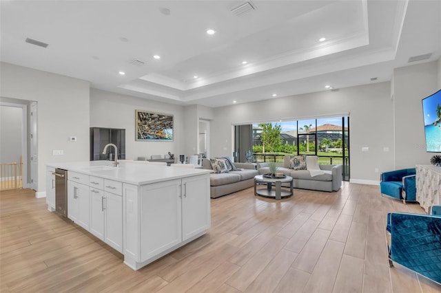 kitchen with a center island with sink, sink, light wood-type flooring, a tray ceiling, and white cabinetry