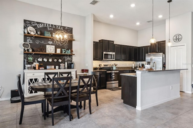 kitchen with dark stone counters, stainless steel appliances, a kitchen island with sink, pendant lighting, and a chandelier