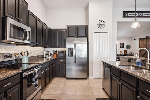 kitchen featuring sink, a barn door, dark stone countertops, light tile patterned floors, and appliances with stainless steel finishes