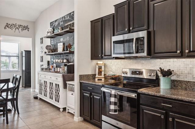 kitchen with stainless steel appliances, dark stone countertops, lofted ceiling, dark brown cabinets, and light tile patterned floors