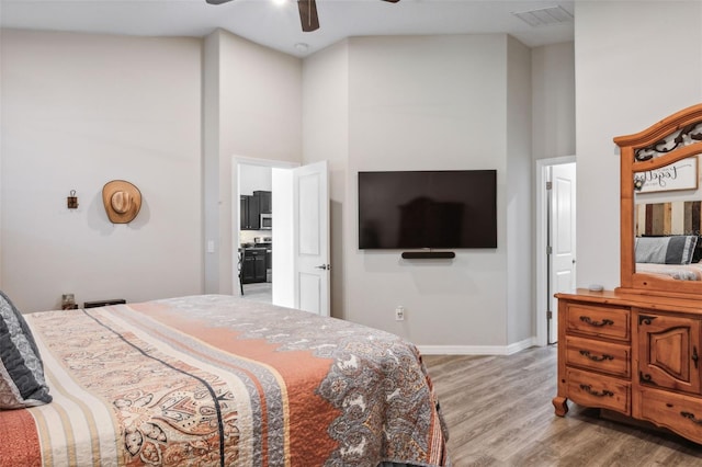 bedroom with ceiling fan, a towering ceiling, and light wood-type flooring