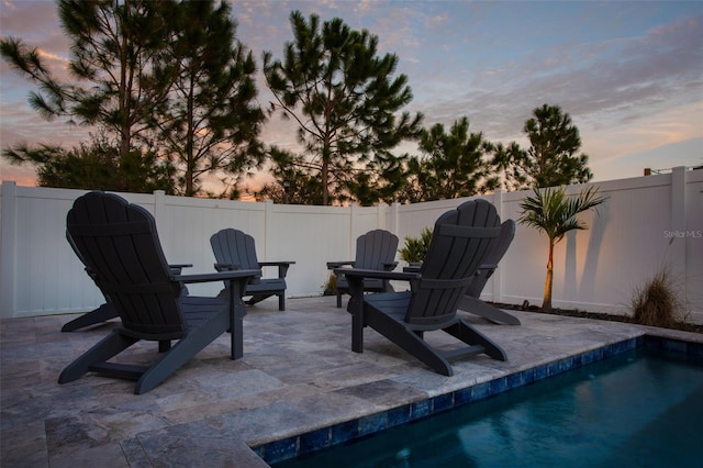 patio terrace at dusk featuring a fenced in pool