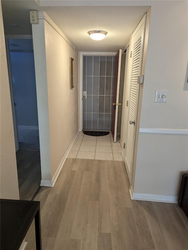 hallway with light wood-type flooring, a textured ceiling, and baseboards