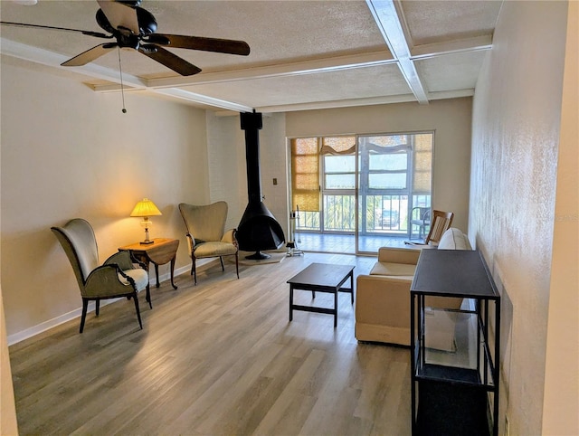 living area featuring beam ceiling, wood finished floors, a wood stove, ceiling fan, and coffered ceiling