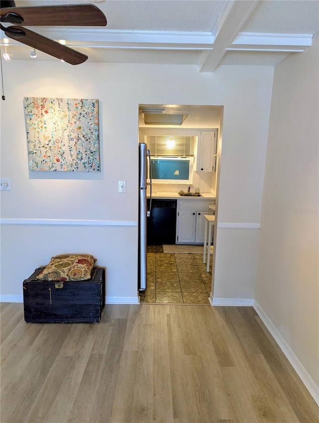 corridor featuring wood finished floors, beam ceiling, baseboards, and a sink