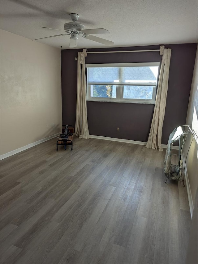 empty room featuring a ceiling fan, wood finished floors, baseboards, and a textured ceiling
