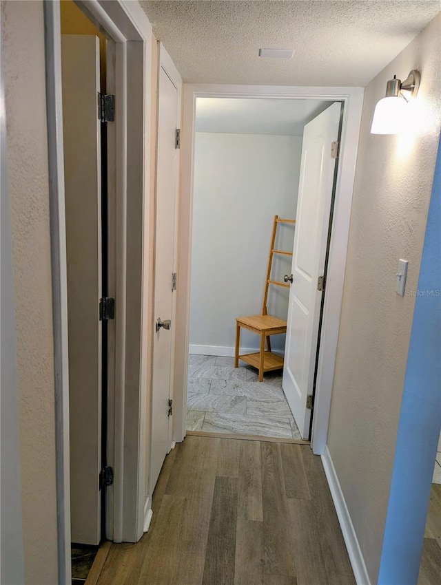 hallway with wood finished floors, a textured ceiling, and baseboards