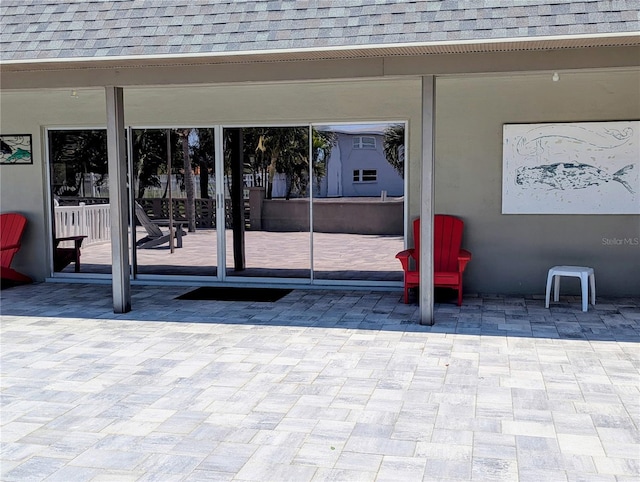 property entrance with a patio area and roof with shingles
