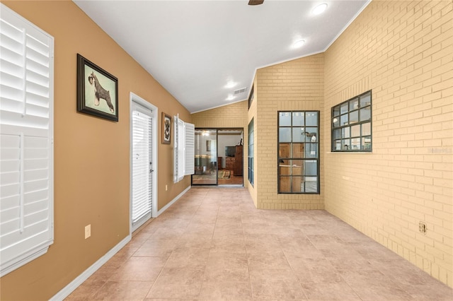 corridor with light tile patterned flooring, brick wall, and vaulted ceiling