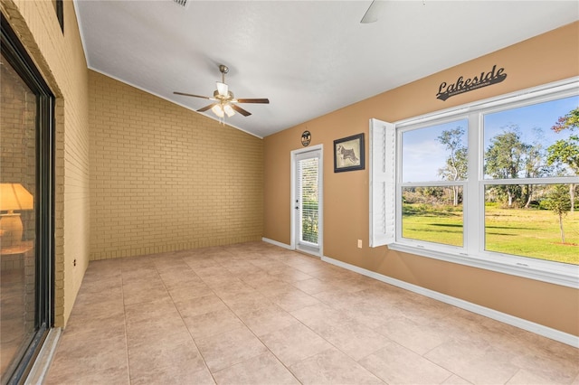 unfurnished room with light tile patterned floors, vaulted ceiling, ceiling fan, and brick wall