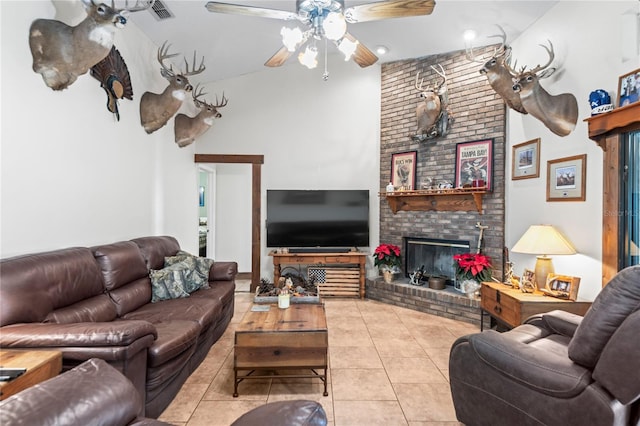 tiled living room featuring ceiling fan, a towering ceiling, and a brick fireplace