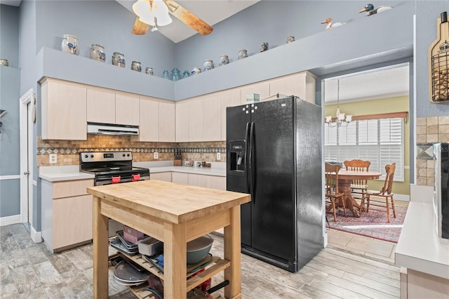 kitchen with black refrigerator with ice dispenser, high vaulted ceiling, light hardwood / wood-style floors, stainless steel electric stove, and ceiling fan with notable chandelier