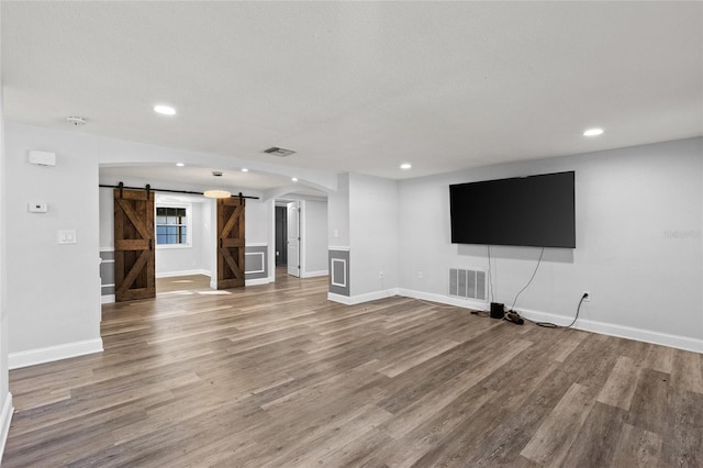 unfurnished living room featuring hardwood / wood-style flooring, a barn door, and a textured ceiling