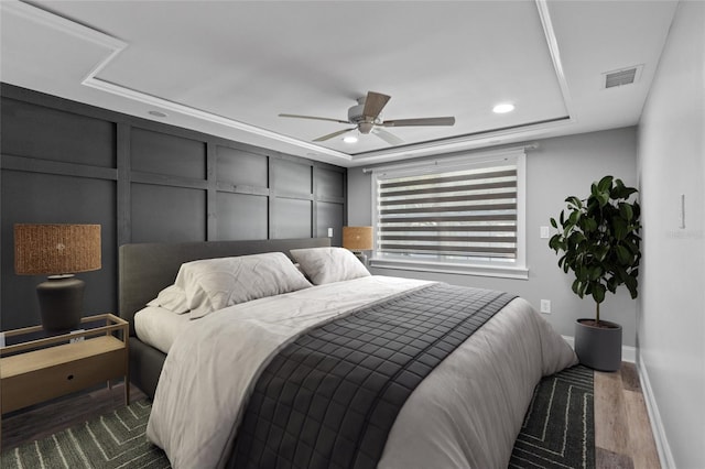 bedroom with a tray ceiling, ceiling fan, and dark wood-type flooring