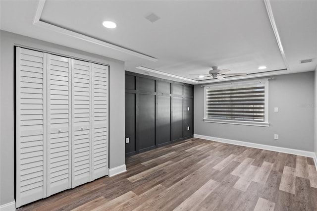 unfurnished bedroom featuring hardwood / wood-style flooring, ceiling fan, and a raised ceiling