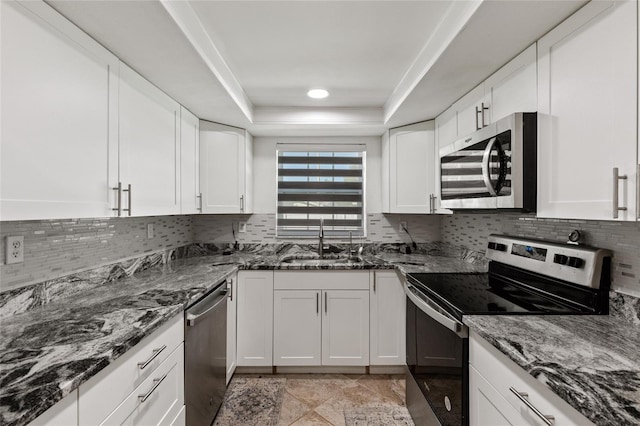 kitchen featuring sink, dark stone counters, a tray ceiling, white cabinets, and appliances with stainless steel finishes