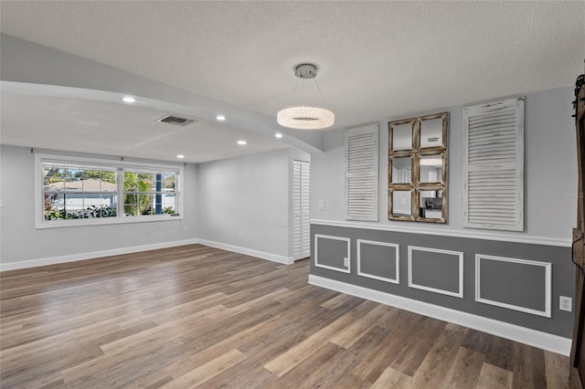 spare room with a barn door, wood-type flooring, and a textured ceiling