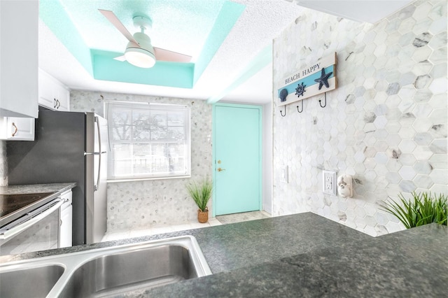 kitchen with a tray ceiling, white cabinetry, ceiling fan, and stainless steel electric range oven